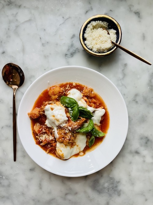 Cauliflower chicken Parmesan in a white bowl with fresh basil.
