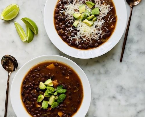 Two white bowls of vegetarian taco soup topped with diced avocado.
