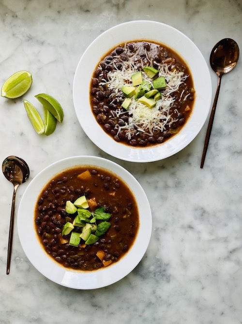 Two white bowls of vegetarian taco soup topped with diced avocado.