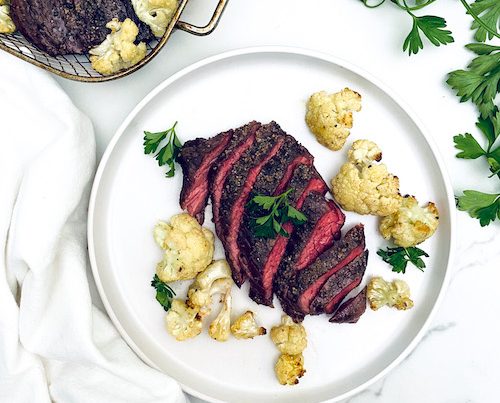 Sliced garlic steak on a plate with roasted cauliflower florets.