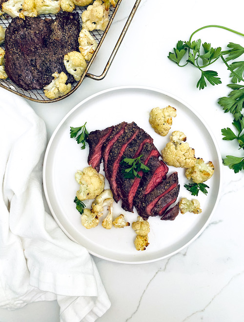 Sliced garlic steak on a plate with roasted cauliflower florets.