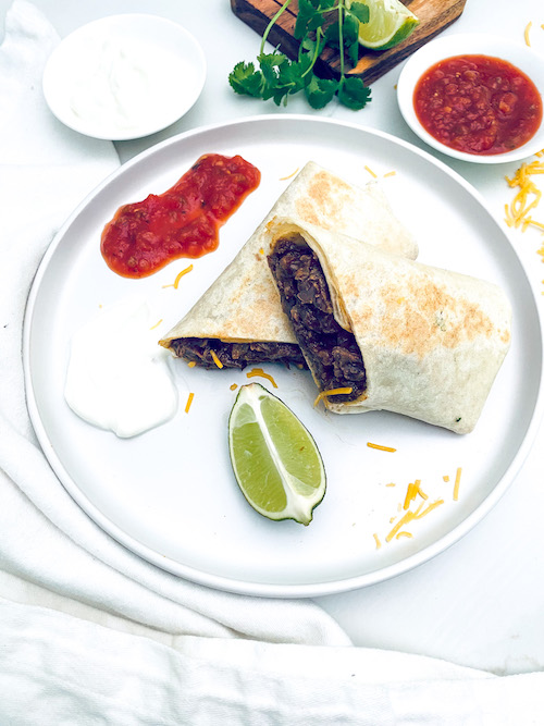 A beef and cheese burrito cut in half on a white dinner plate.
