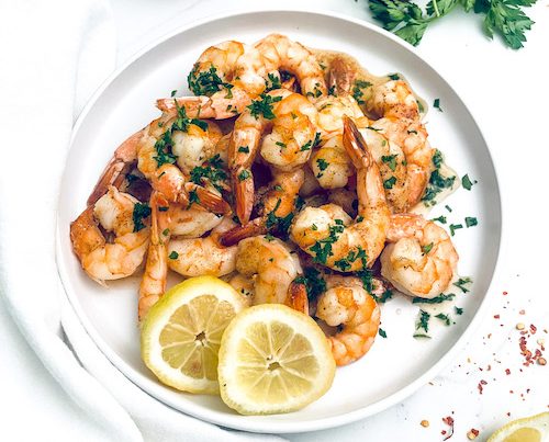 A pile of Cajun butter shrimp on a plate with lemon slices.