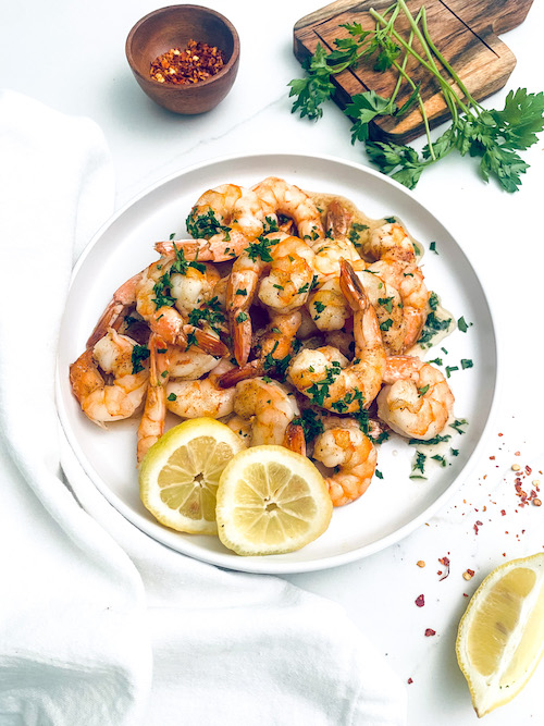 A pile of Cajun butter shrimp on a plate with lemon slices.