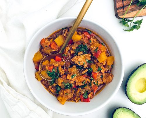 Ground turkey and cubed squash chili with a spoon in a white bowl.
