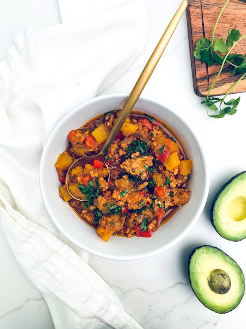 Ground turkey and cubed squash chili with a spoon in a white bowl.