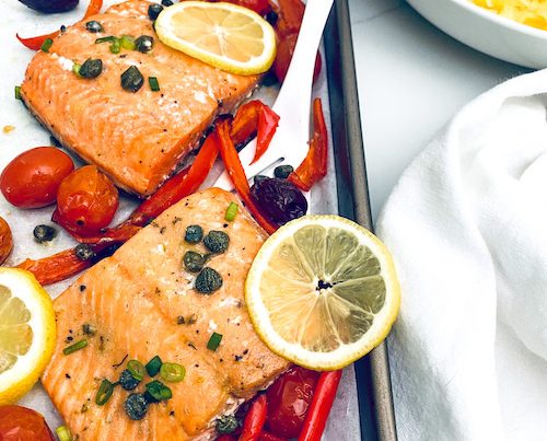 Salmon fillets with red peppers and tomatoes on a sheet pan.