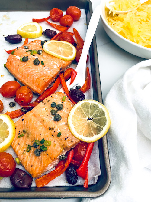 Salmon fillets with red peppers and tomatoes on a sheet pan.