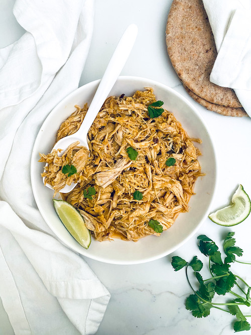 Shredded tandoori chicken in a white bowl with lime wedges.