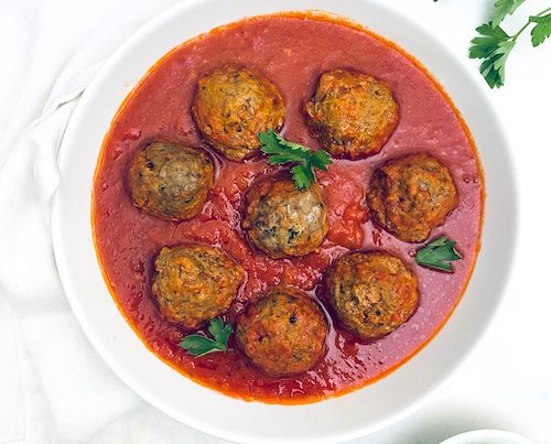 Zucchini meatballs in a bowl of marinara sauce.