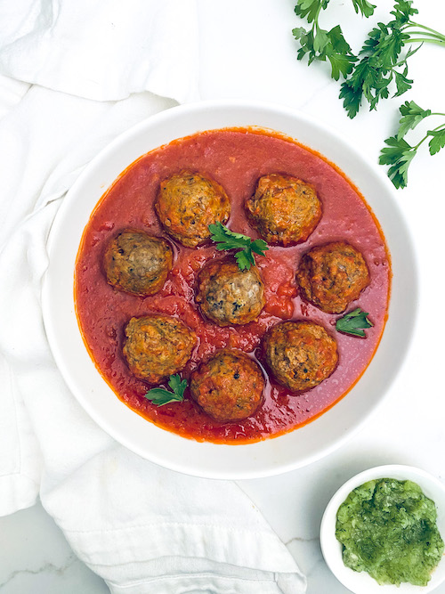 Zucchini meatballs in a bowl of marinara sauce.