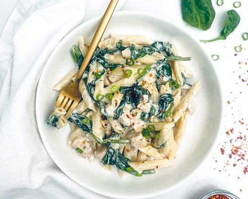 Chicken ranch pasta with spinach in a white serving bowl.