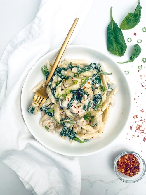 Chicken ranch pasta with spinach in a white serving bowl.