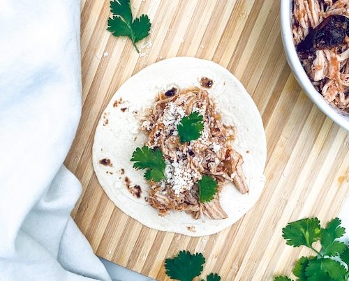 Pulled chicken Tinga on a flour tortilla on a wooden cutting board.