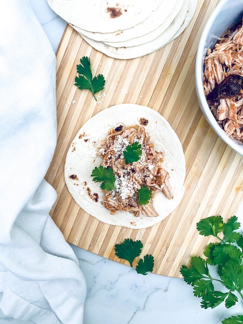 Pulled chicken Tinga on a flour tortilla on a wooden cutting board.