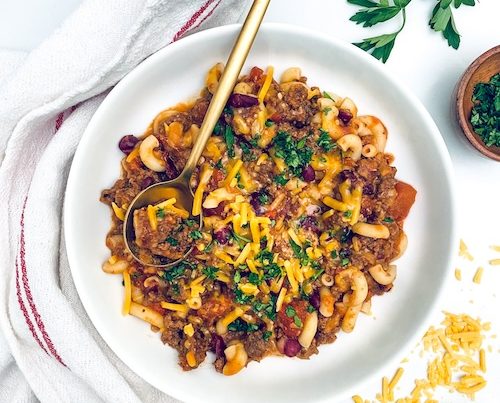 Chili Mac in a bowl topped with shredded cheese.