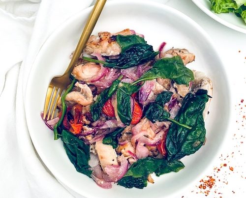 Greek chicken with wilted spinach in a white bowl.