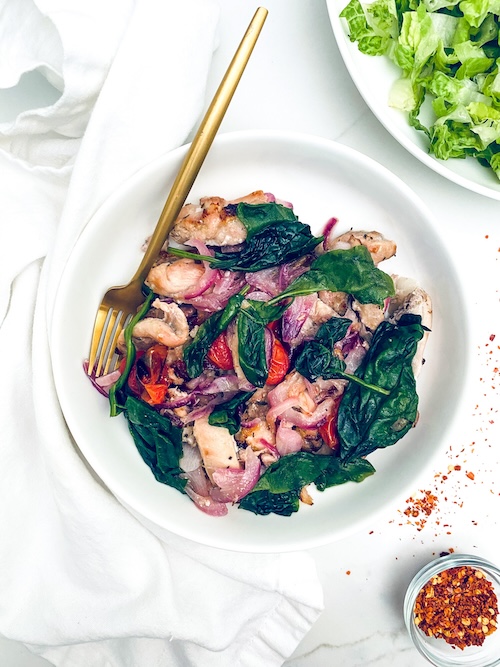 Greek chicken with wilted spinach in a white bowl.