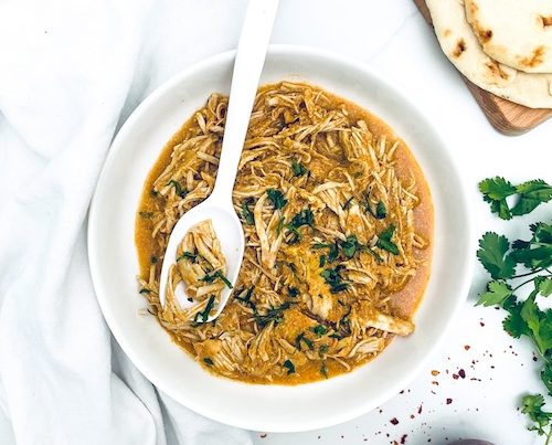 Pulled chicken masala with parsley in a white serving bowl.