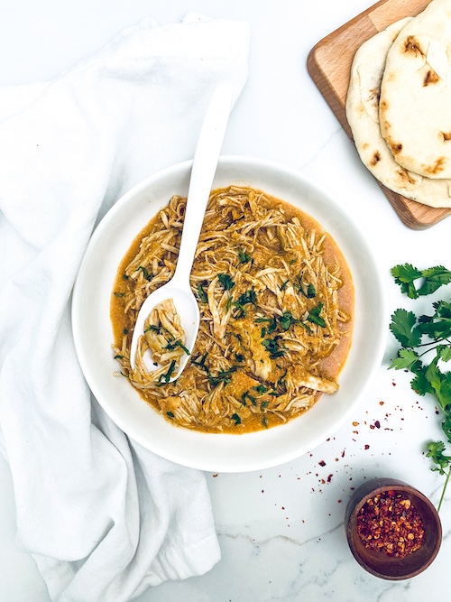 Pulled chicken masala with parsley in a white serving bowl.