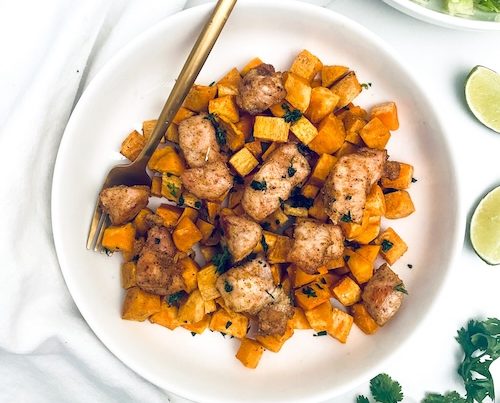 Diced chicken with cubed butternut squash on a white dinner plate with a fork.