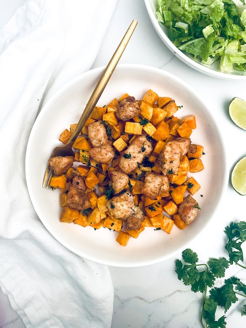 Diced chicken with cubed butternut squash on a white dinner plate with a fork.