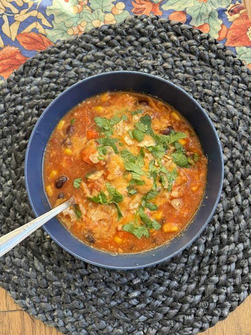 A bowl of chicken tortilla soup with a spoon.