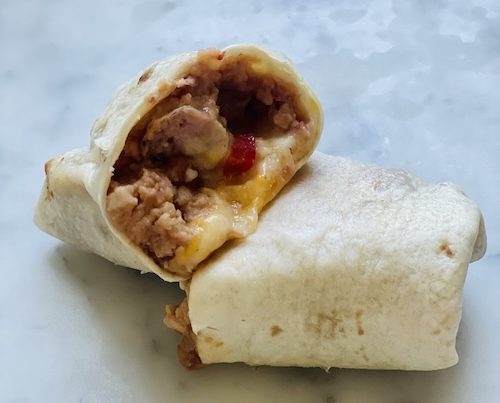 A breakfast sausage and bean burrito cut in half.