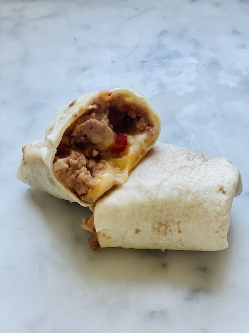 A breakfast sausage and bean burrito cut in half.
