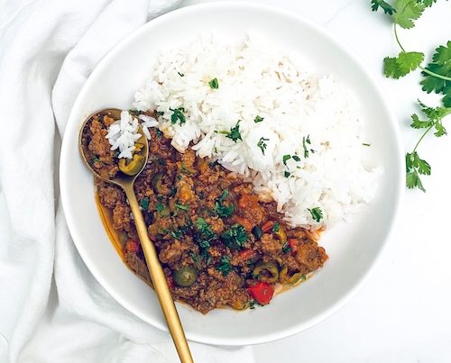 Cuban picadillo next to white rice in a bowl.