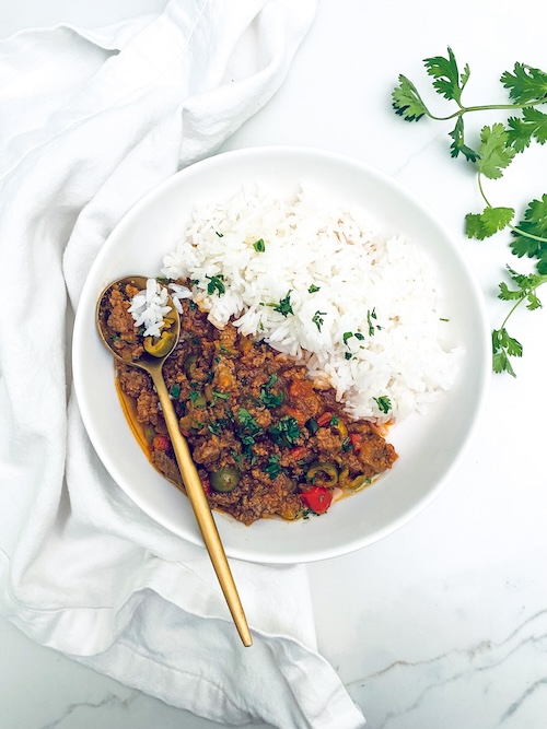 Cuban picadillo next to white rice in a bowl.