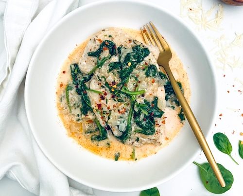 Mary me spinach chicken in a white bowl with a fork.