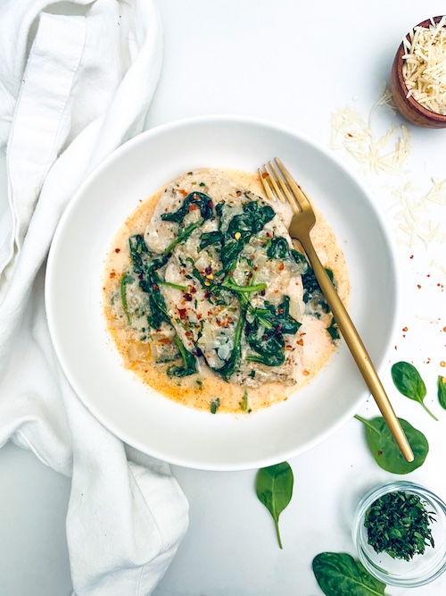 Mary me spinach chicken in a white bowl with a fork.