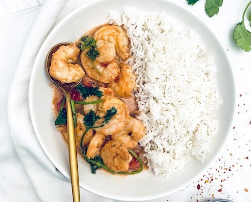 Indian butter shrimp and rice on a white plate.
