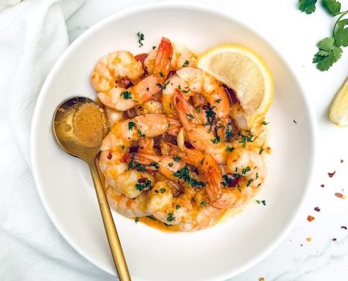 Spicy garlic shrimp in a bowl with lemon wedges.