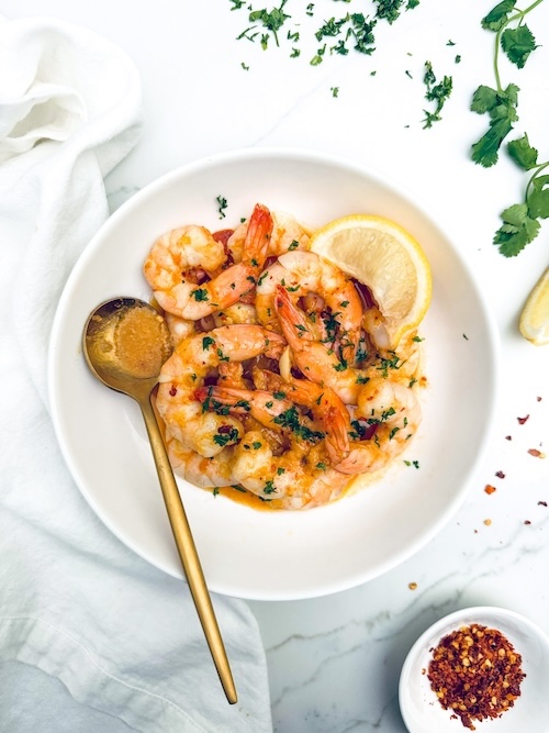 Spicy garlic shrimp in a bowl with lemon wedges.