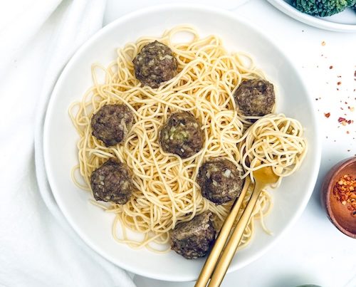 Pesto meatballs over a plate of spaghetti.