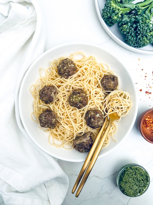 Pesto meatballs over a plate of spaghetti.
