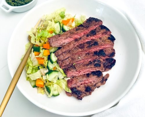 Sliced skirt steak with green salad on a plate.