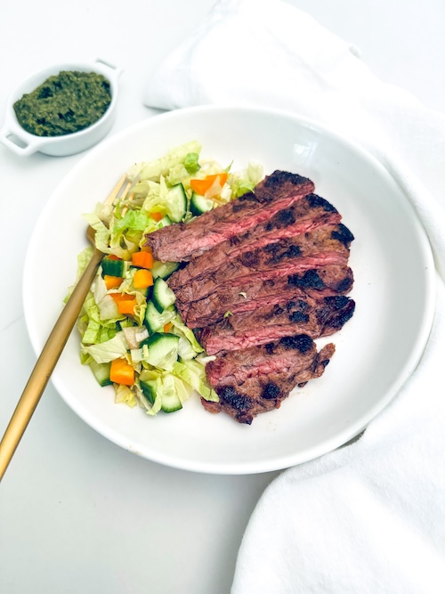 Sliced skirt steak with green salad on a plate.