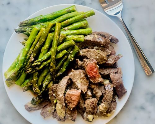 Buttered steak and asparagus on a plate.