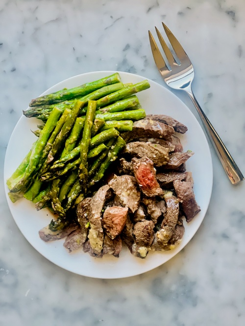 Buttered steak and asparagus on a plate.