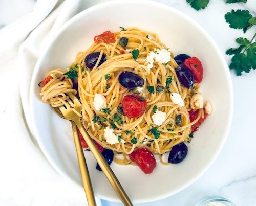 Spaghetti with tomatoes and olives in a bowl.
