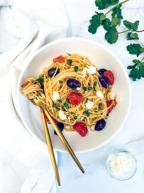 Spaghetti with tomatoes and olives in a bowl.