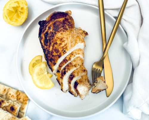 Yogurt marinated chicken breast with lemon on a plate.