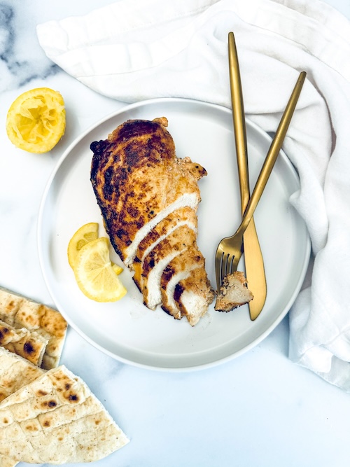 Yogurt marinated chicken breast with lemon on a plate.