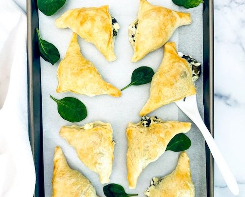 Puff pastry filled with spinach and feta on a baking pan.