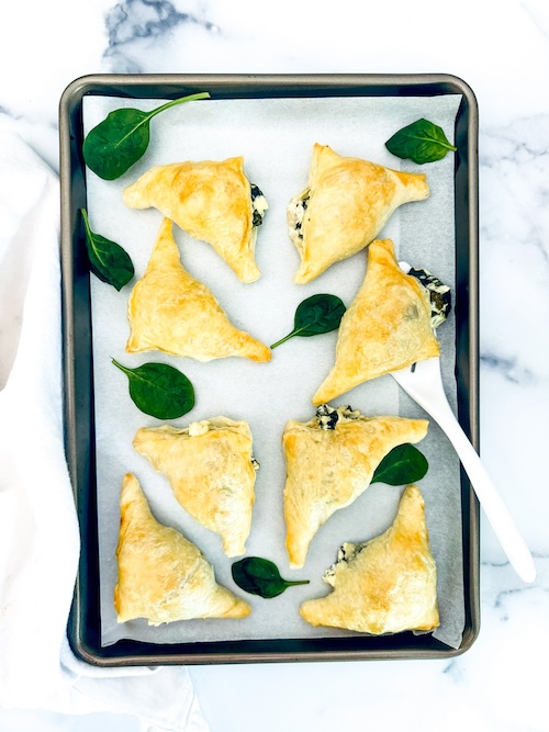 Puff pastry filled with spinach and feta on a baking pan.