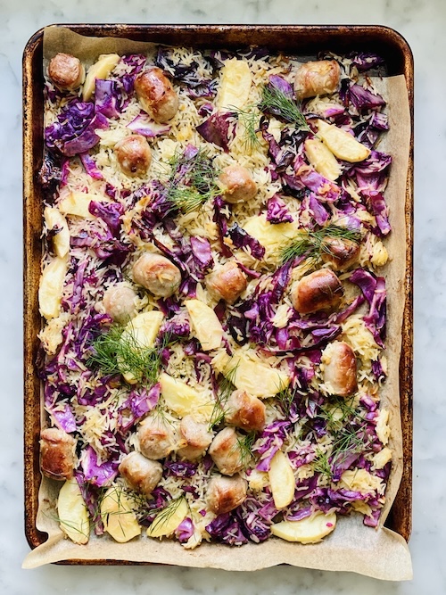 A sheet pan filled with bratwurst and apples.