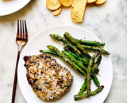 Everything bagel pork chop on a plate with green beans.
